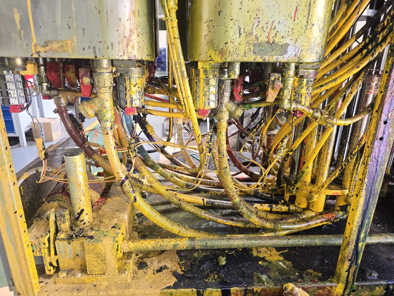 Stainer dosing machine before the upgrade — close-up of heavily contaminated hoses, fittings, filters and red-handled valves buried beneath the canisters